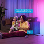 Two people sitting on a couch with a floor lamp, using a device to change the lamp color.